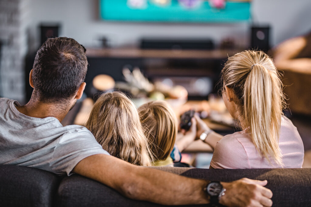 Familj tittar på tv i en soffa. Foto: Istock/Skynesher